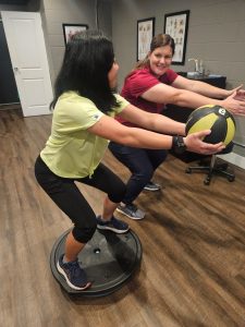 Physical Therapist helps women in a yellow shirt squat on a bosu for balance and strength